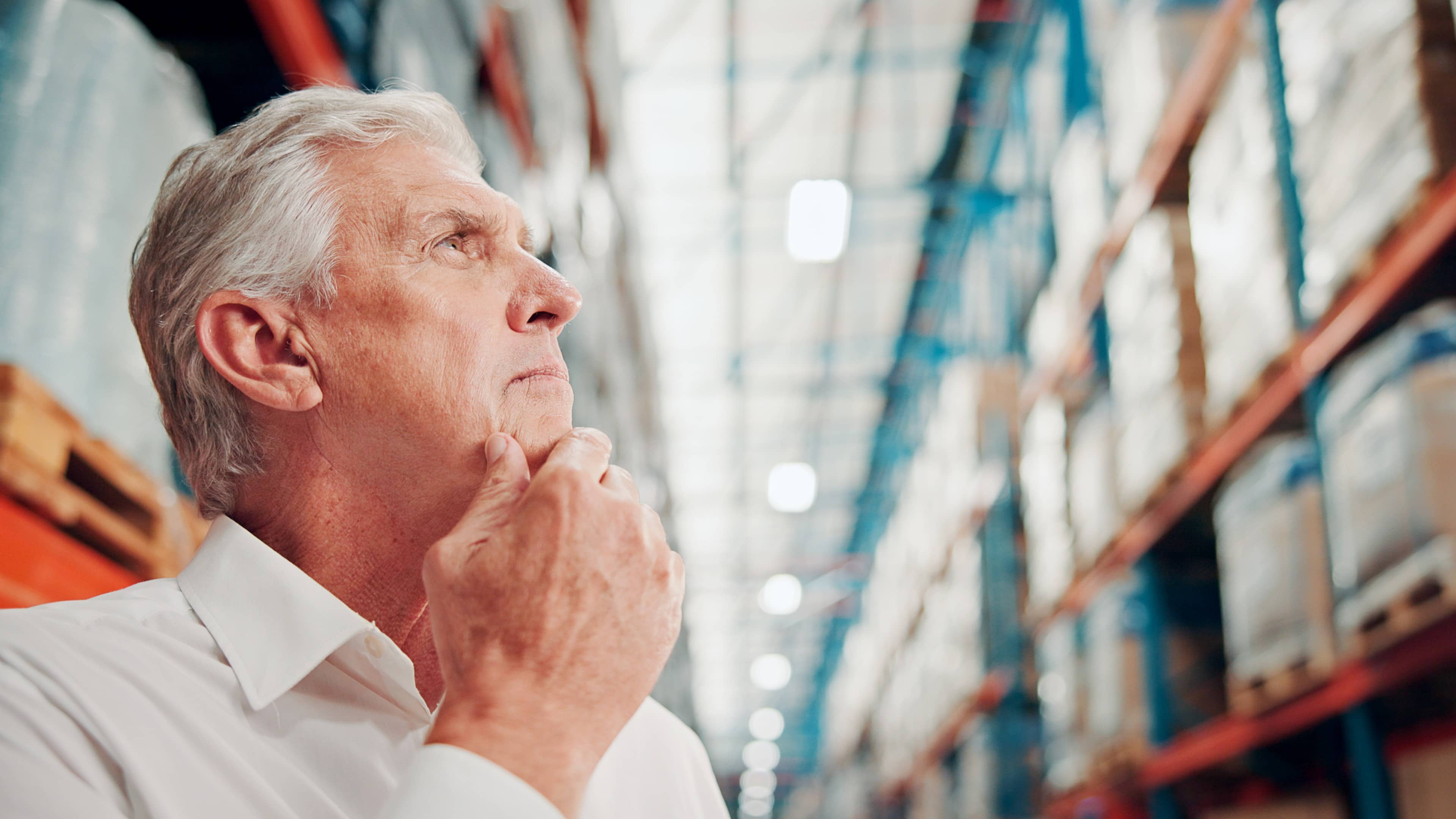 Pensive Senior Businessman Inspecting Inventory in a Large Industrial Warehouse